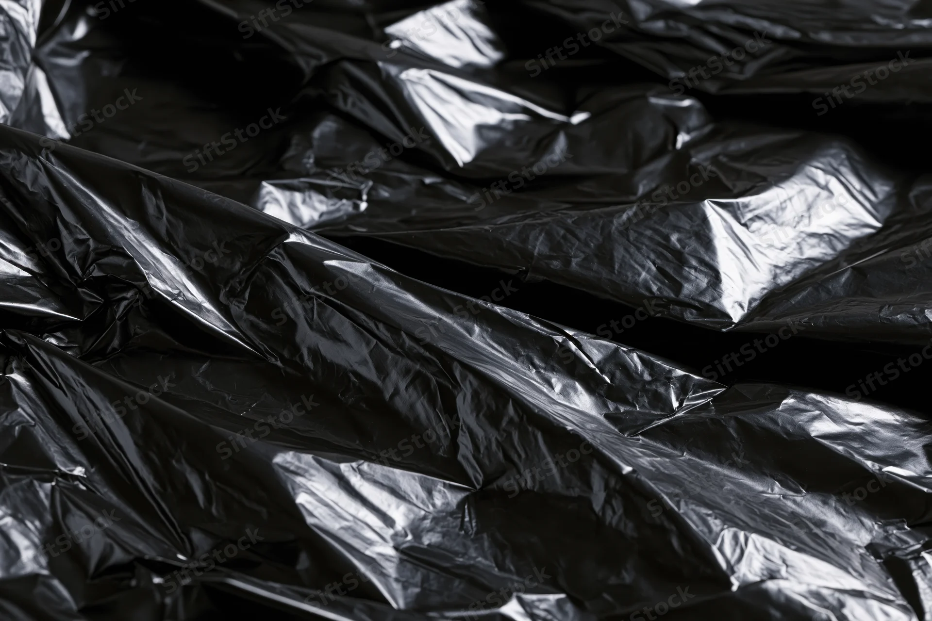 Crumpled black plastic sheeting filling the frame with glossy folds and creases