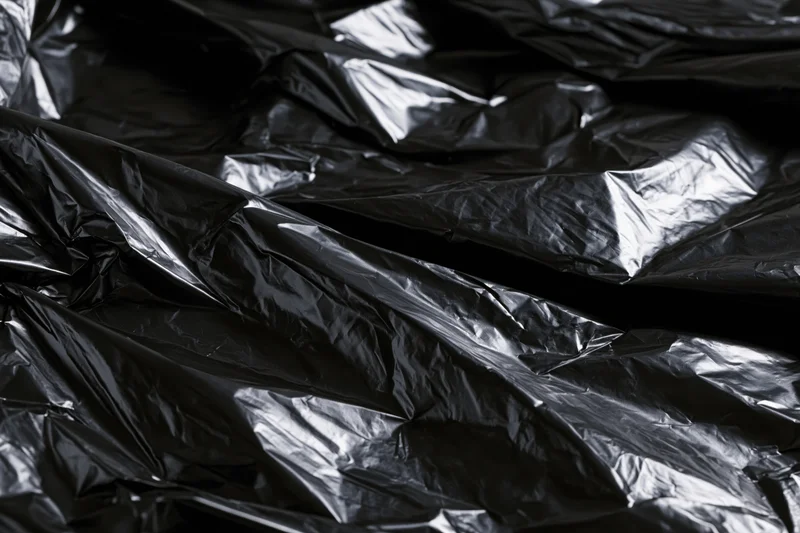 Crumpled black plastic sheeting filling the frame with glossy folds and creases