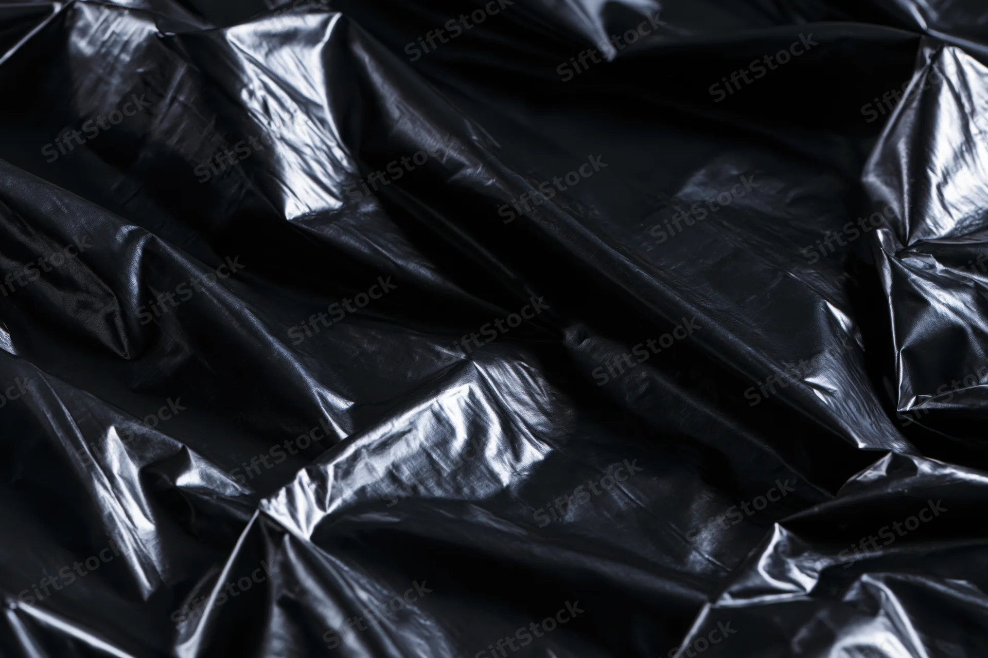 Crumpled black plastic sheeting filling the frame with folds and reflective highlights