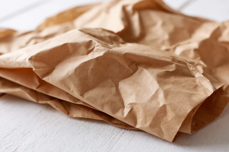 Crumpled brown kraft paper sheets lying flat on a white wooden surface