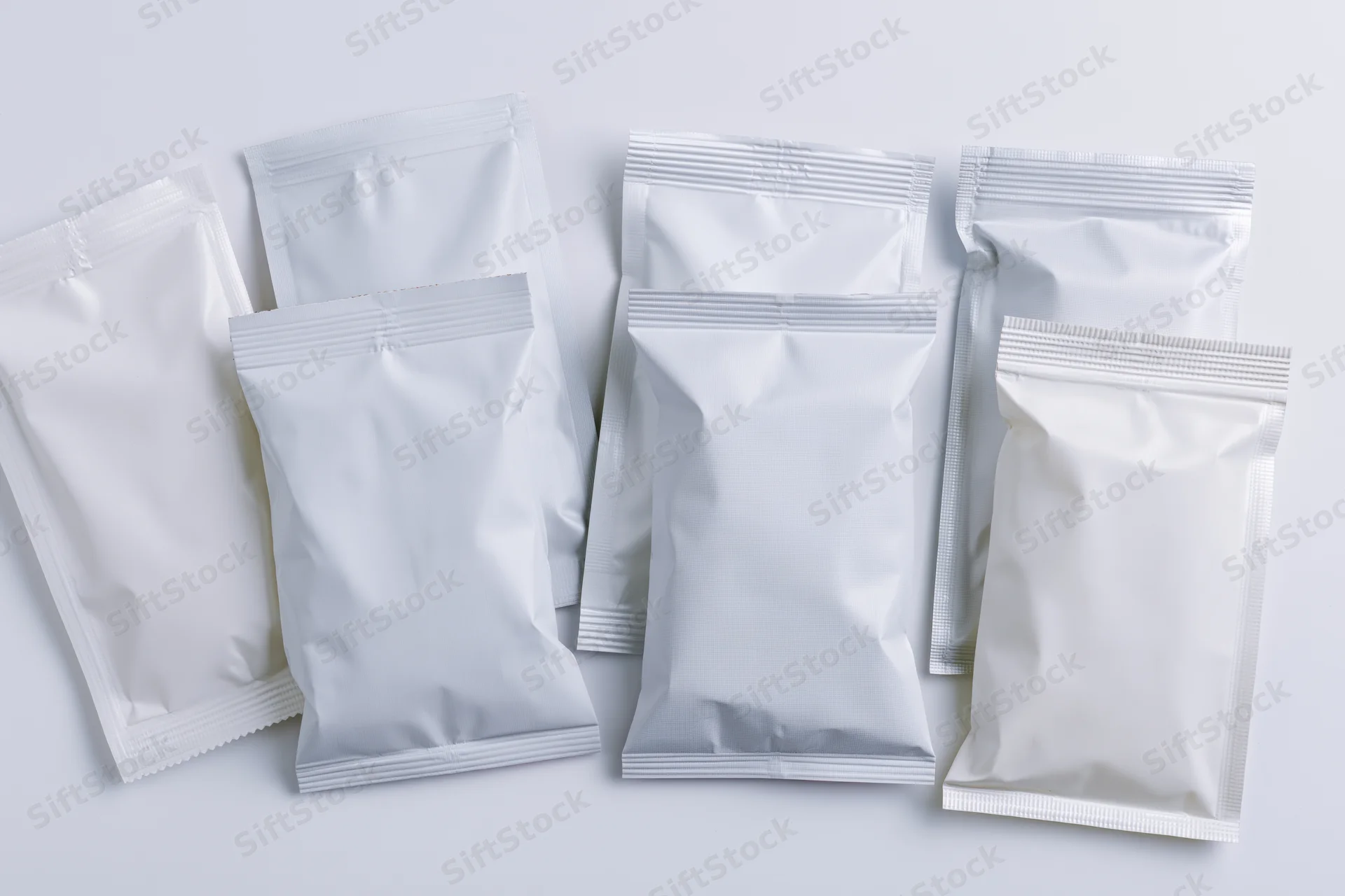 Eight blank white foil and plastic snack pouches arranged in a flat overhead view on a white surface