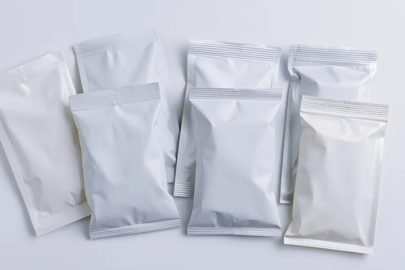 Eight blank white foil and plastic snack pouches arranged in a flat overhead view on a white surface