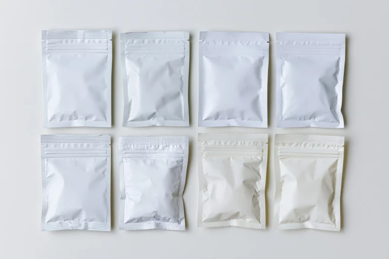 Eight blank white foil and plastic snack pouches arranged in two rows on a plain surface