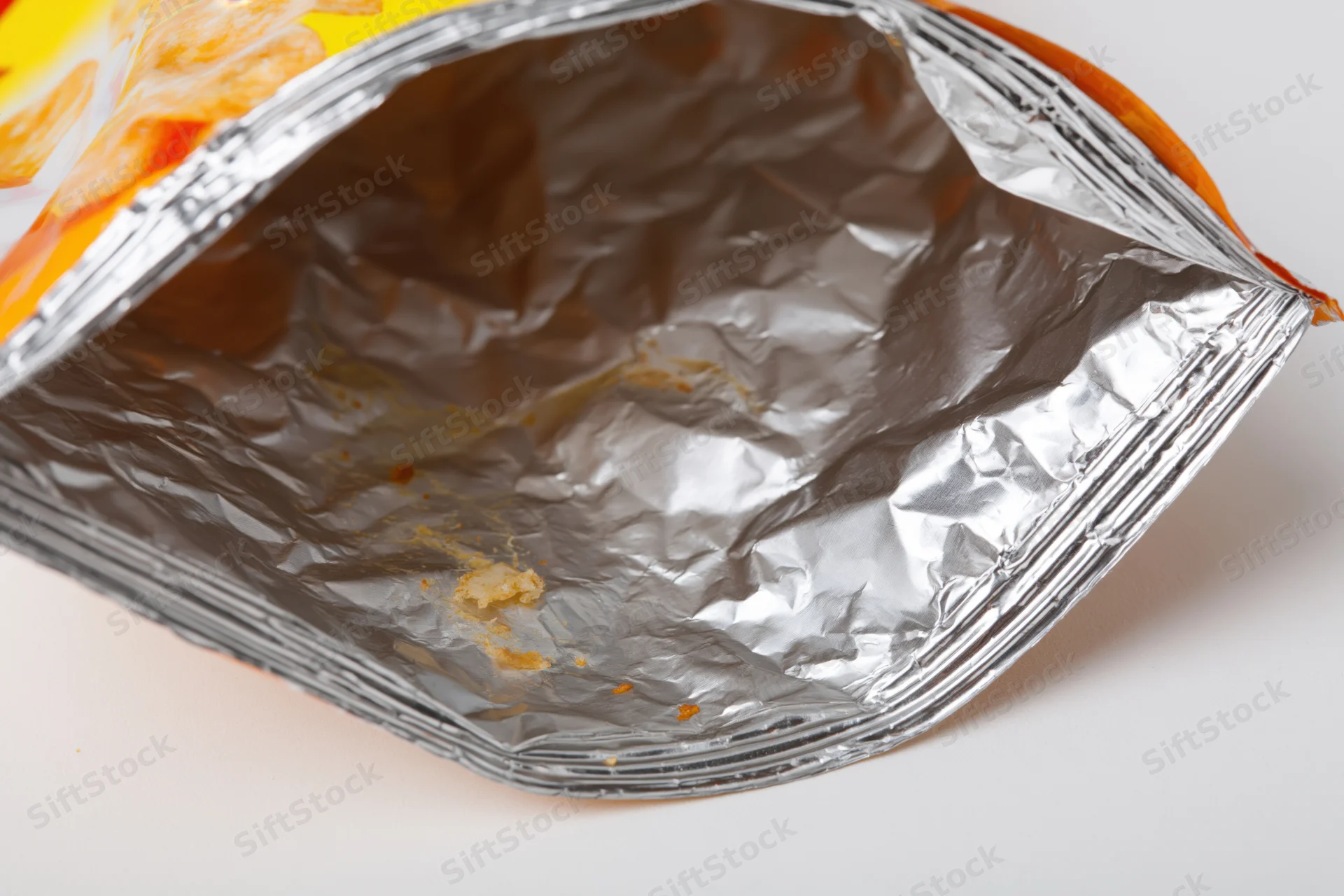 Empty opened chip bag interior showing crumpled foil and crumbs on white surface