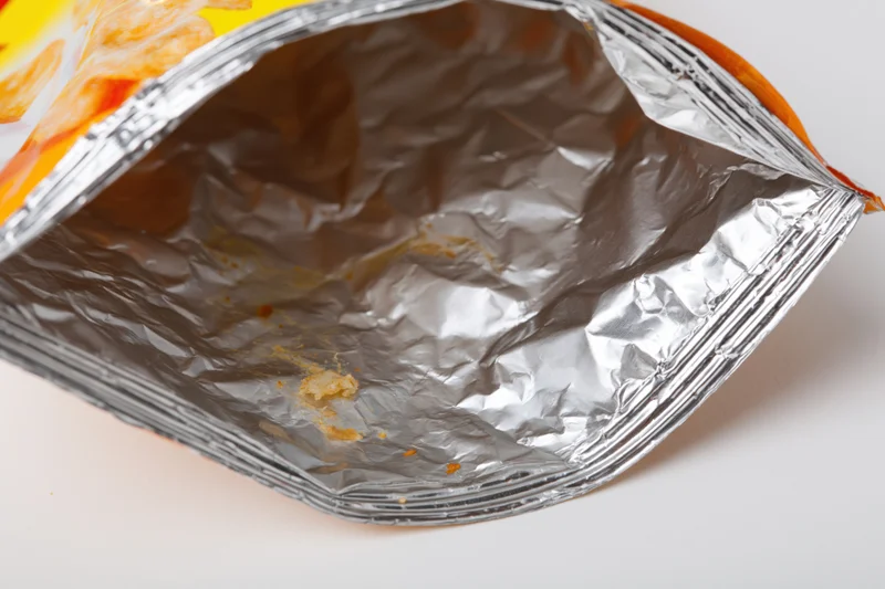 Empty opened chip bag interior showing crumpled foil and crumbs on white surface