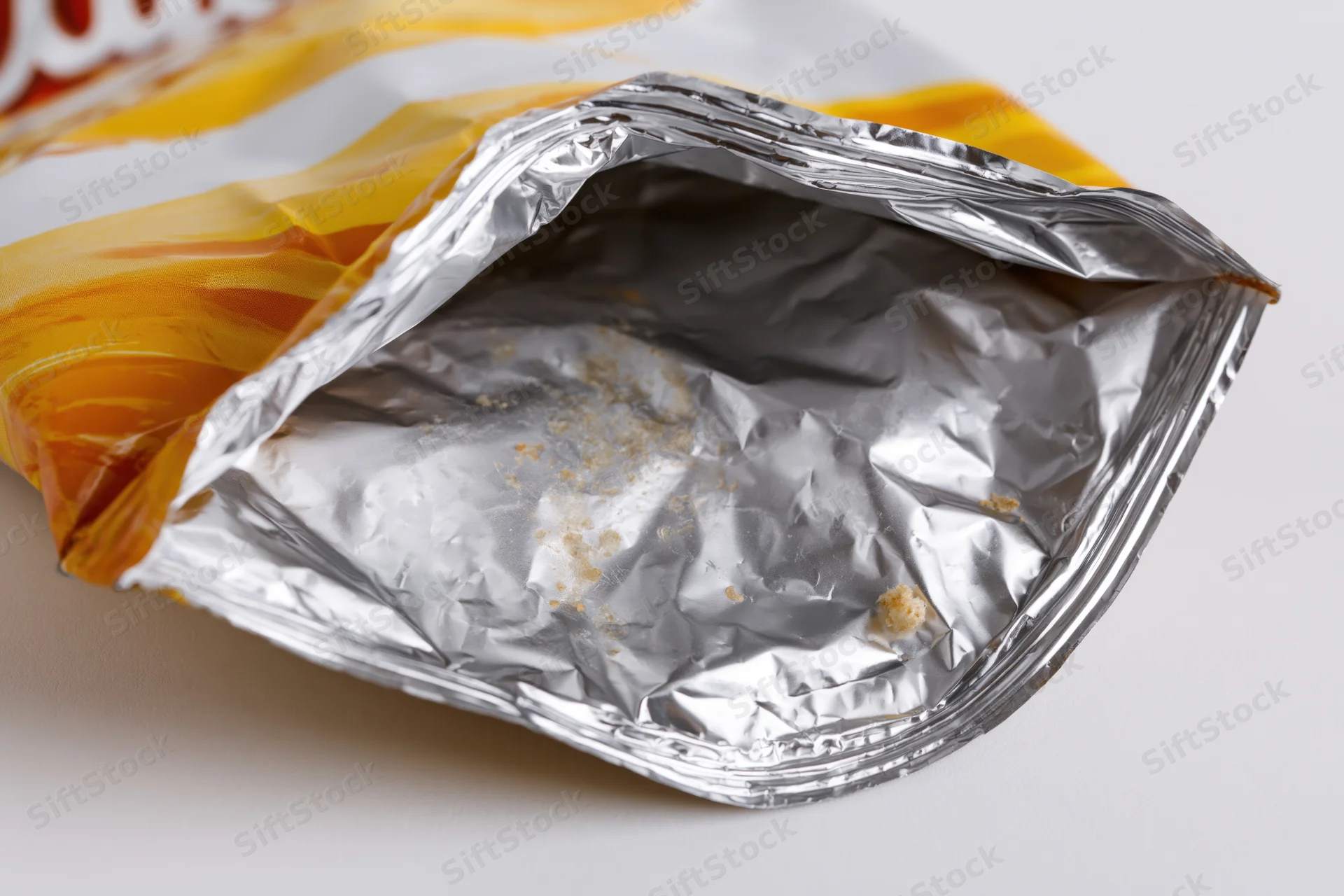 Empty opened chip bag lying on its side showing crumpled aluminum interior with crumbs and residue