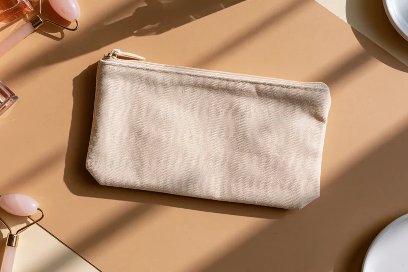 Cream canvas zip pouch centered on warm surface with beauty tools and copyspace
