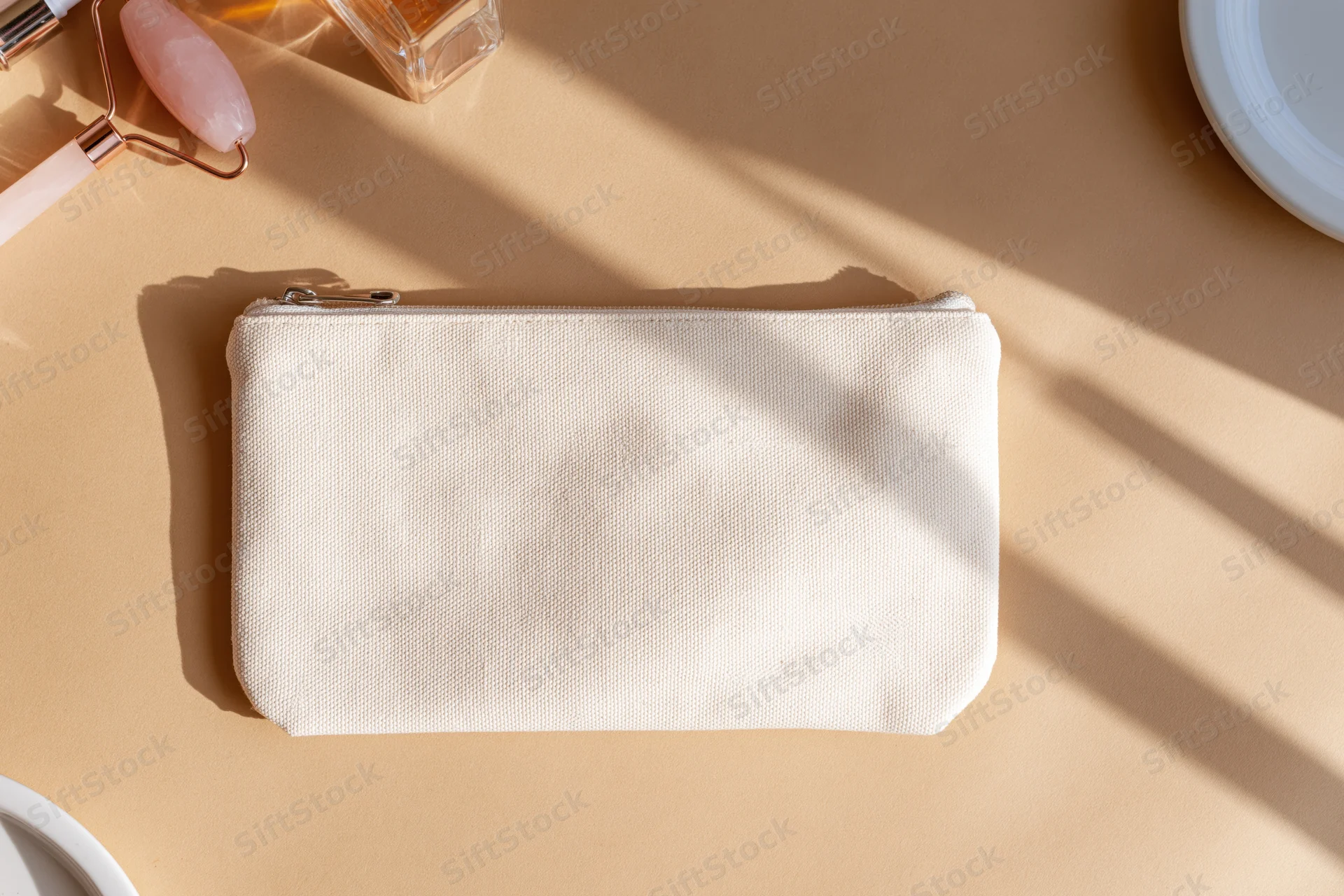 Cream canvas zip pouch centered on warm beige surface with beauty tools and sunlight shadows