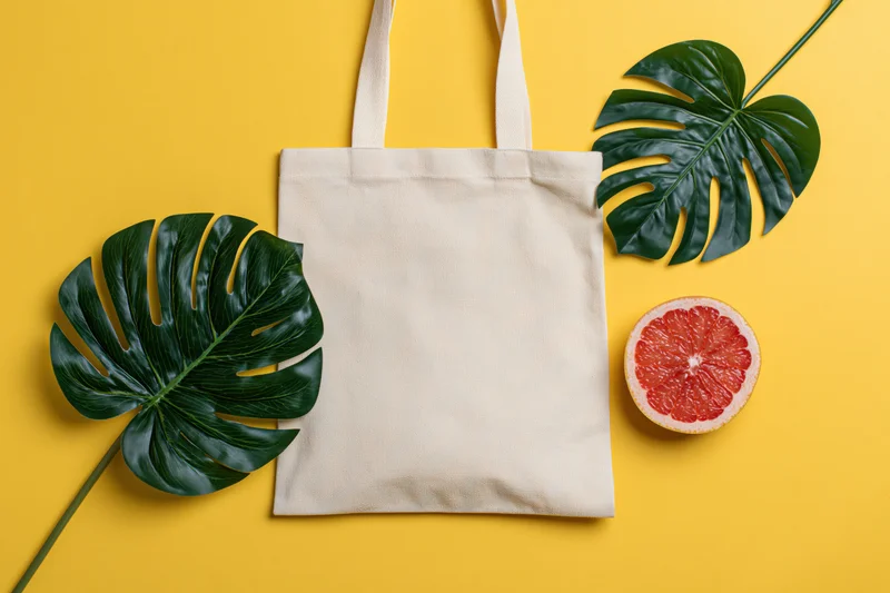 Plain canvas tote bag with monstera leaves and grapefruit slice on yellow background