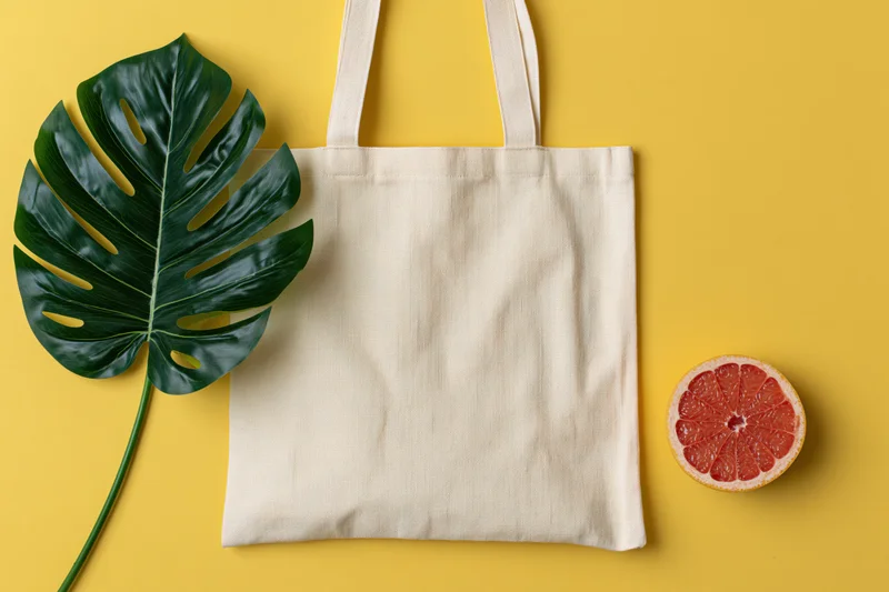 Plain canvas tote bag with monstera leaf and grapefruit slice on yellow surface