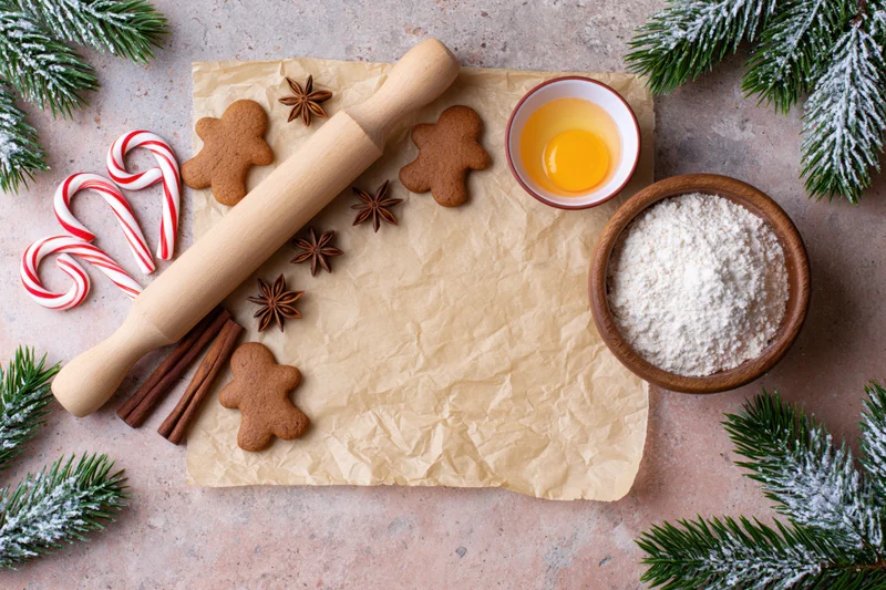 Gingerbread cookies and baking ingredients arranged on parchment with evergreen branches and candy canes for christmas baking
