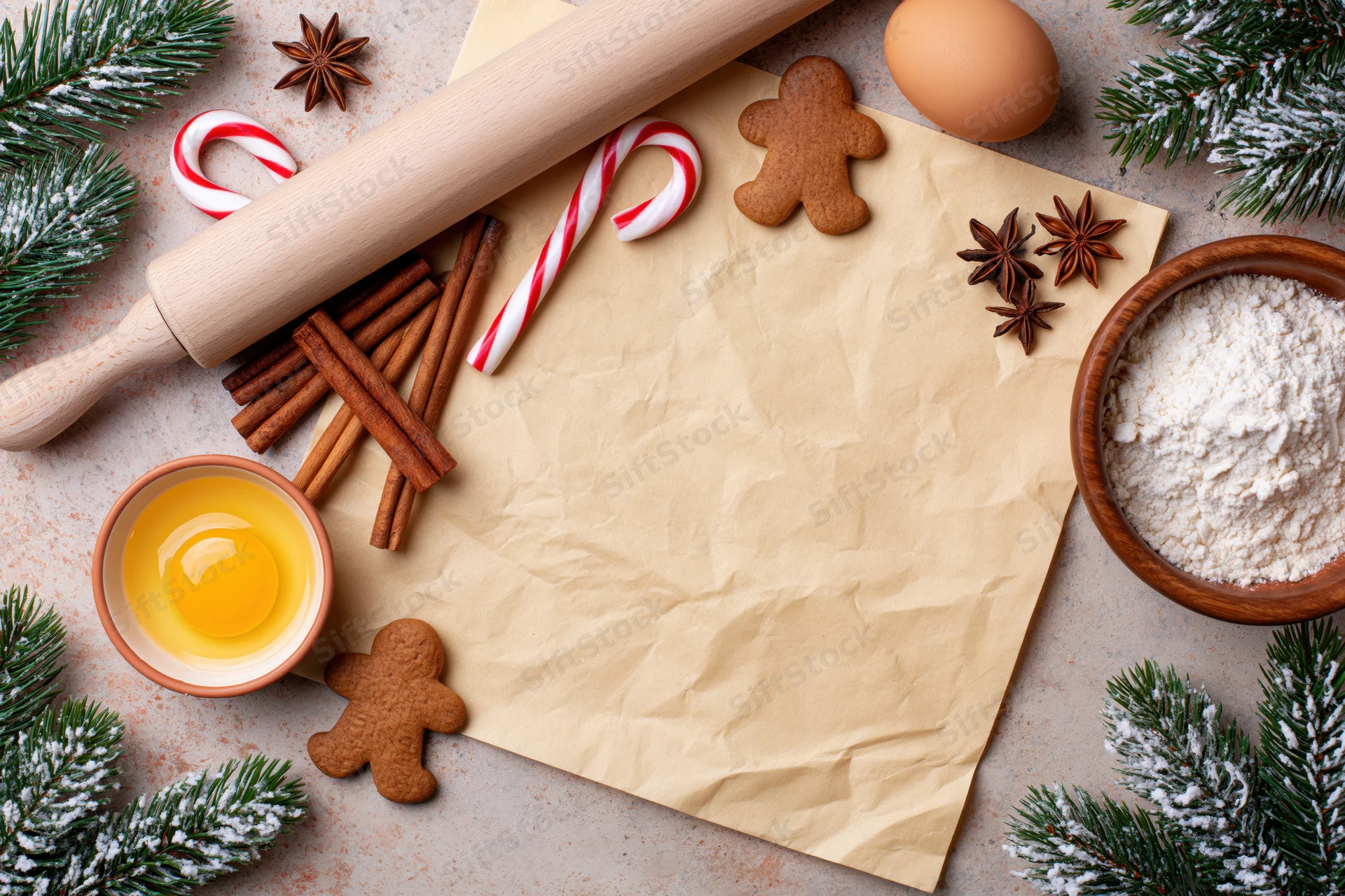 Holiday baking ingredients arranged around crumpled parchment paper on countertop with evergreen branches and candy canes