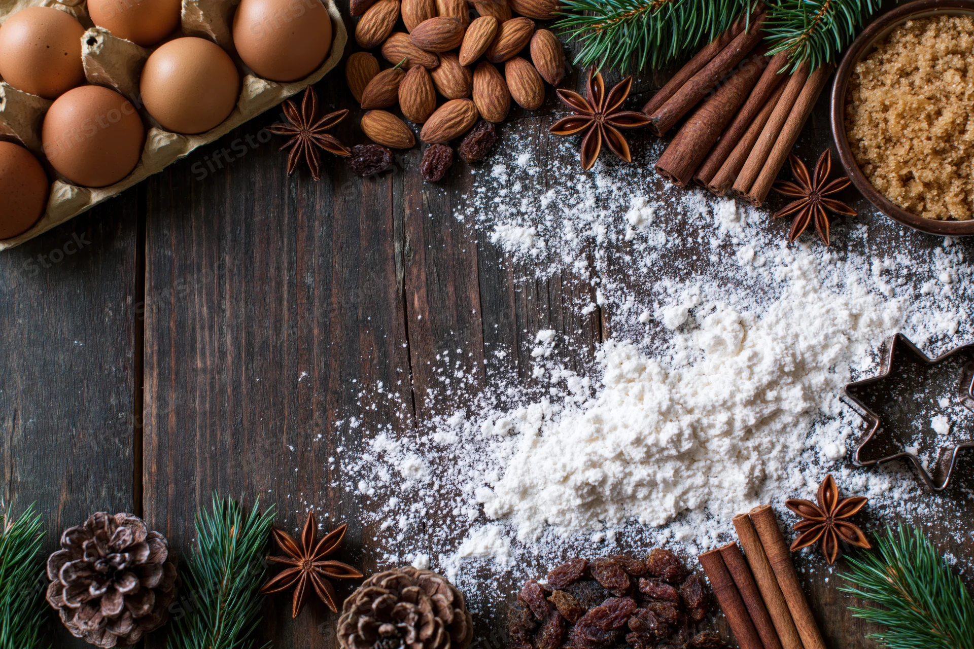 Holiday baking ingredients arranged in a border on a wooden table with flour in the center