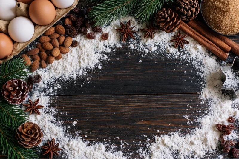 Holiday baking ingredients arranged in a border around a dark wooden table with copyspace in center