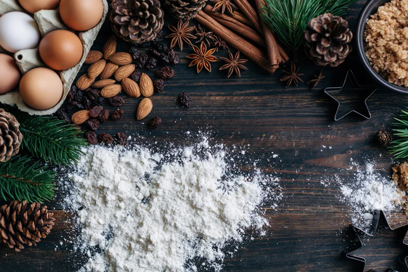Holiday baking ingredients arranged as a border on a dark wooden table