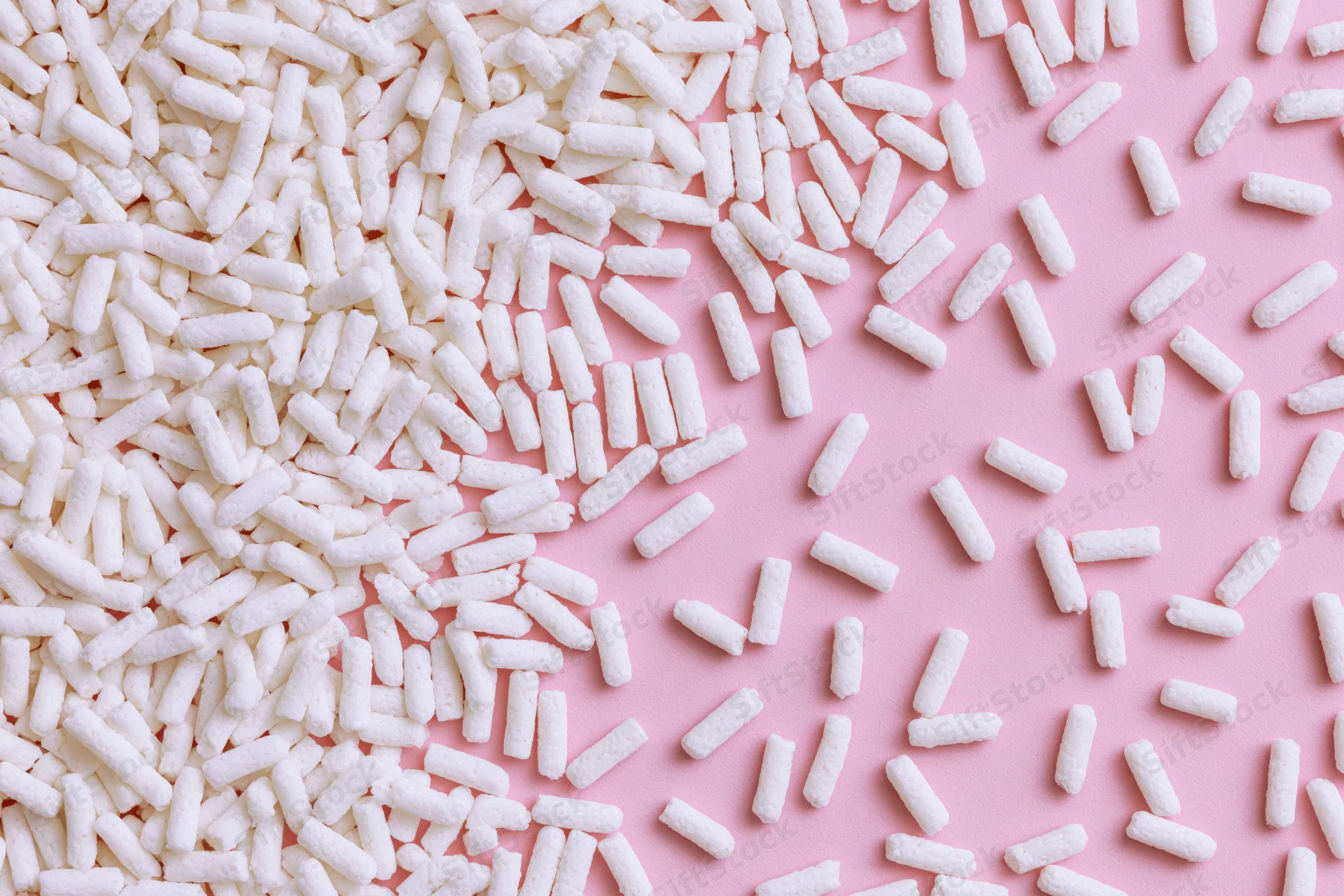 Scattered white sugar sprinkles on pink background in flat lay arrangement
