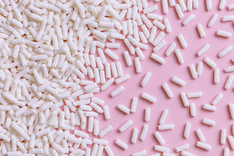 Scattered white sugar sprinkles on pink background in flat lay arrangement