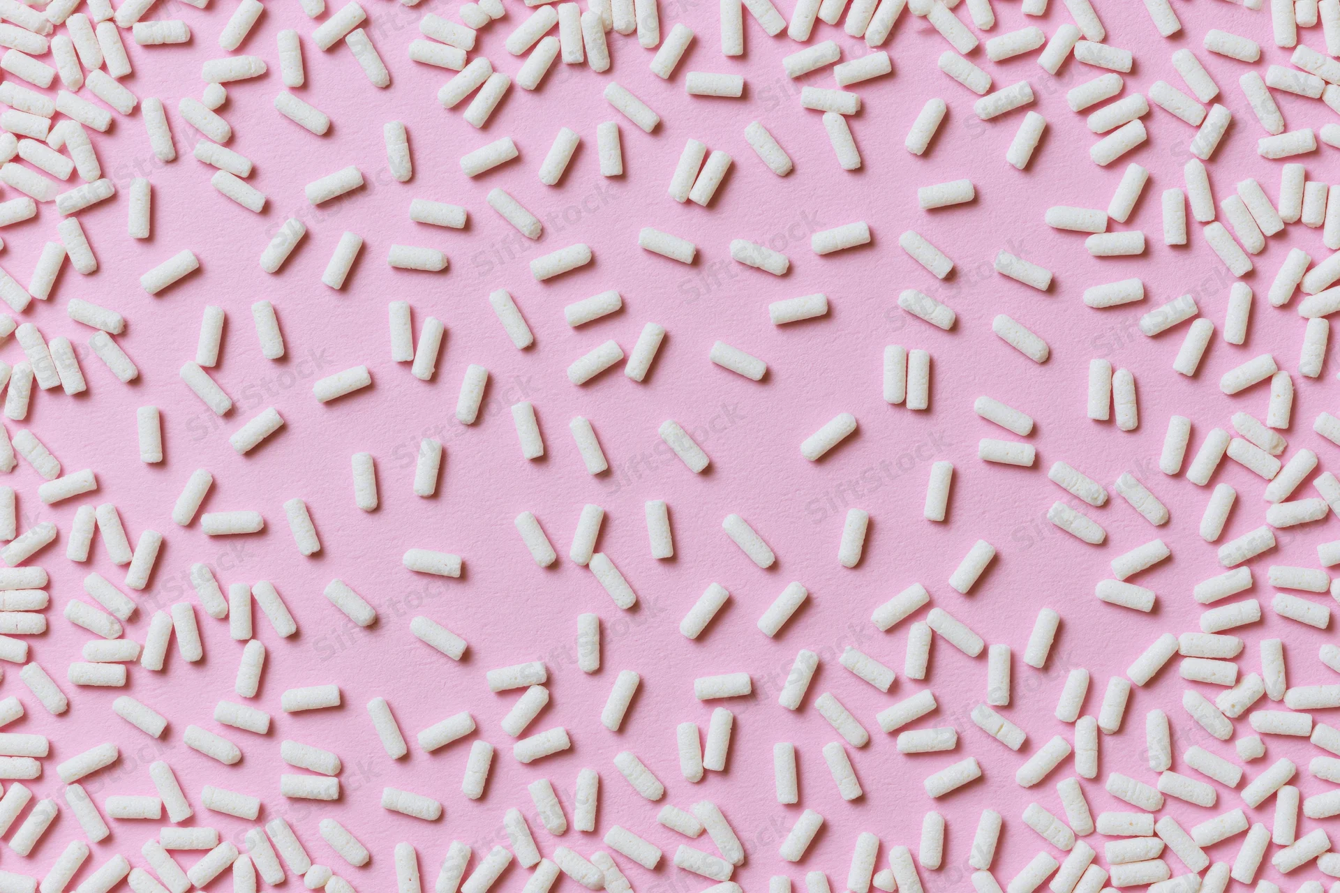 Scattered white sugar sprinkles on pink background in flat lay arrangement