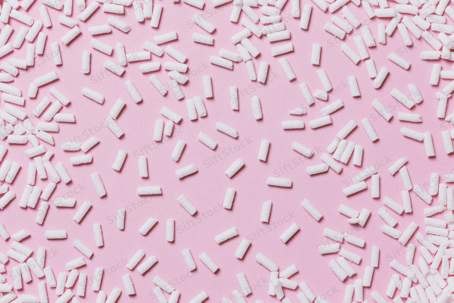 Scattered white sugar sprinkles on pink background