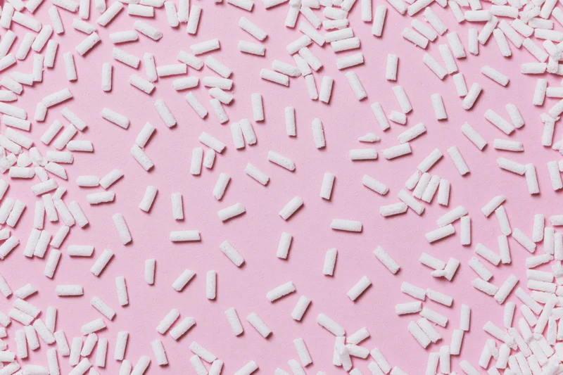 Scattered white sugar sprinkles on pink background
