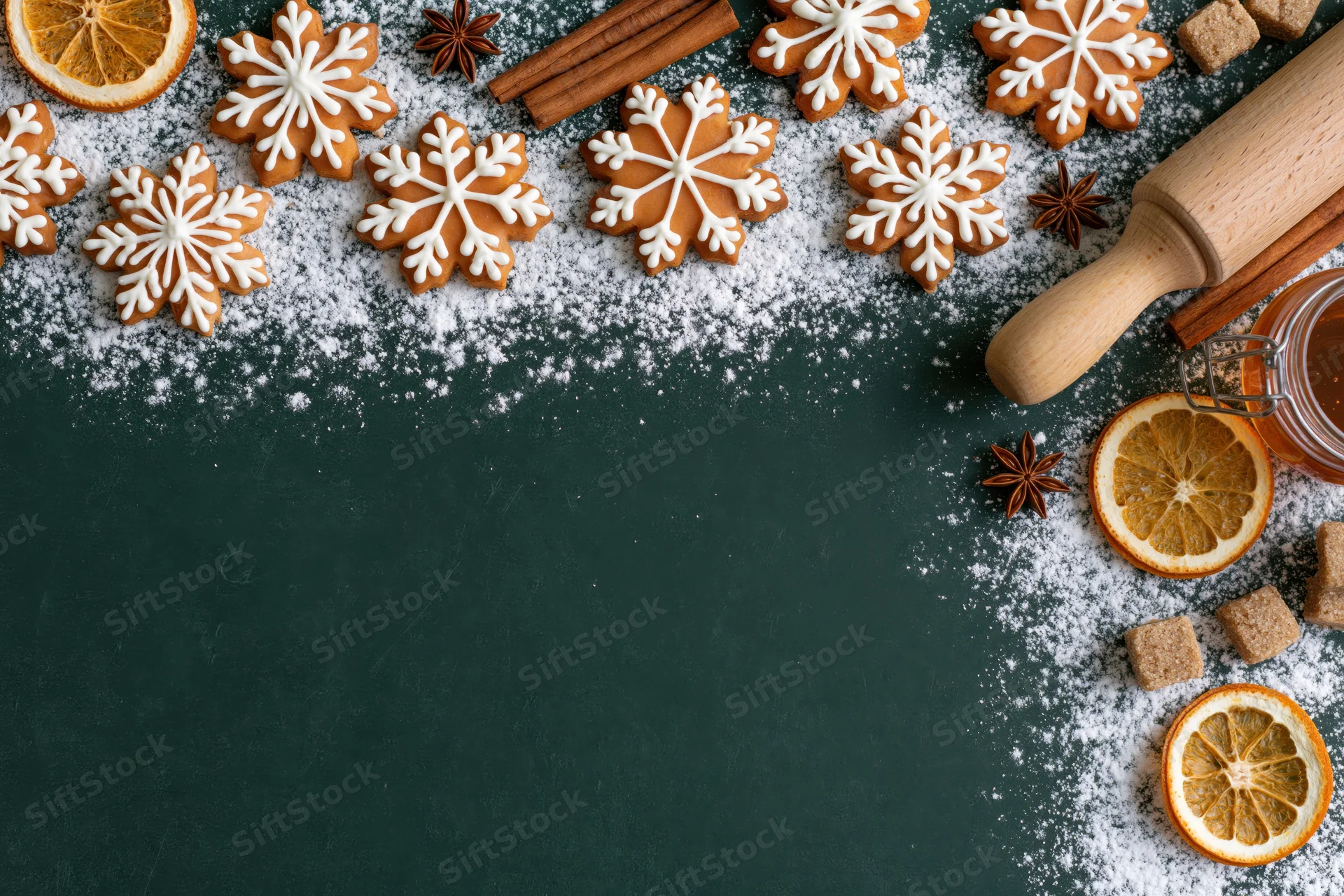 Snowflake-shaped gingerbread cookies with cinnamon and dried orange on dark surface, dusted with powdered sugar, flat lay arrangement with copyspace