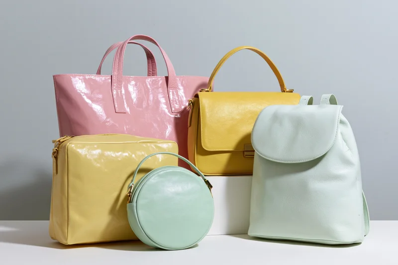 Four women's handbags in pastel colors arranged on a white surface in a studio setting