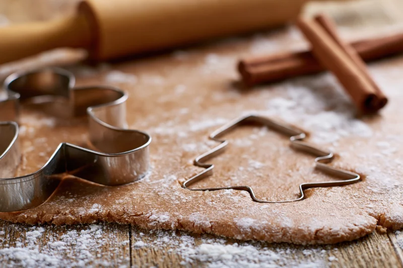 Gingerbread dough rolled flat on a floured wooden surface with cookie cutters and cinnamon sticks