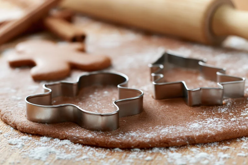 Gingerbread dough being cut with metal cookie cutters on a floured wooden surface