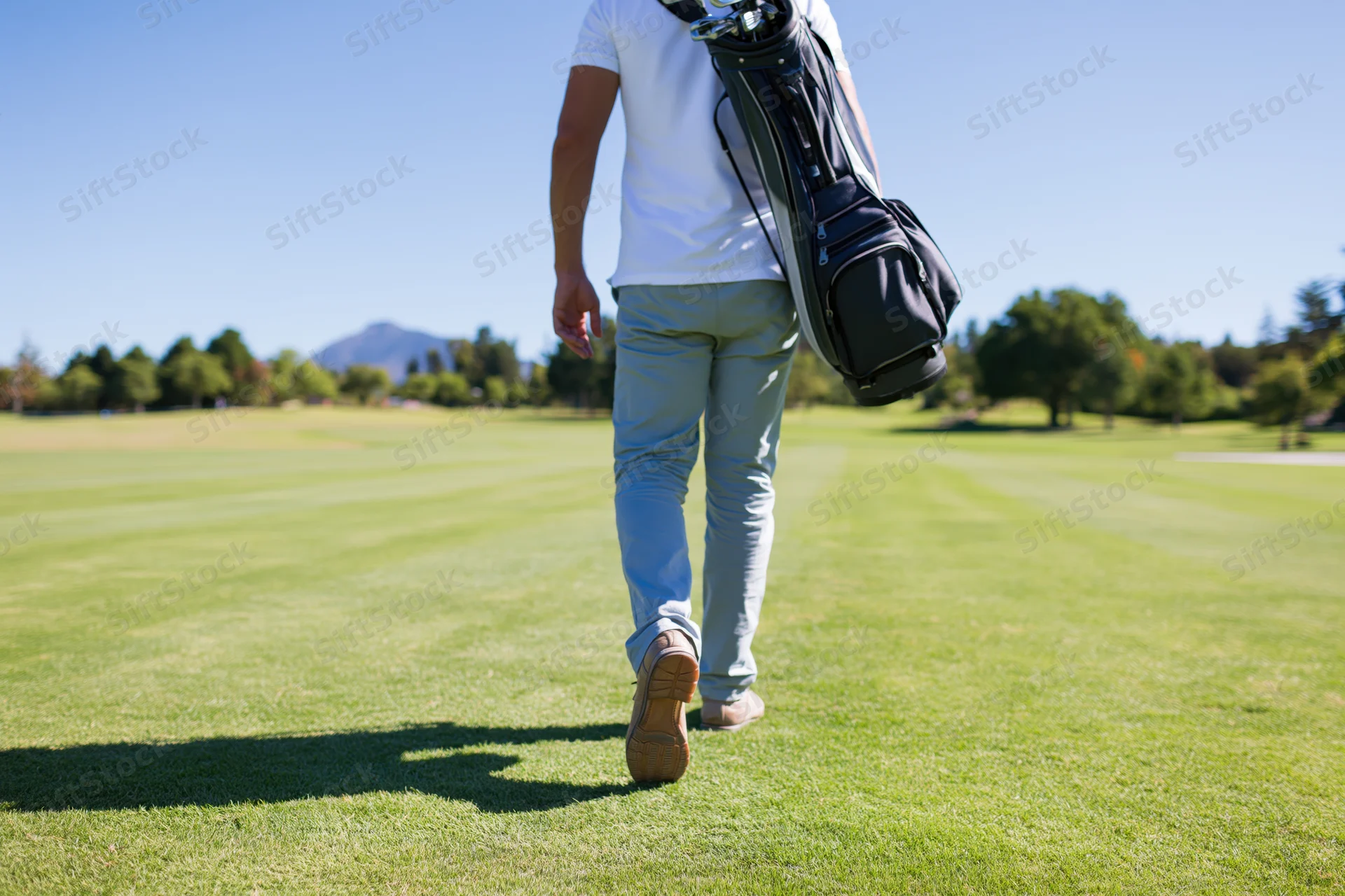 Man walking across a golf course fairway carrying a golf bag