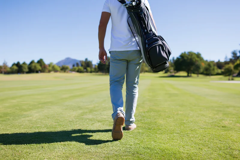 Man walking across a golf course fairway carrying a golf bag