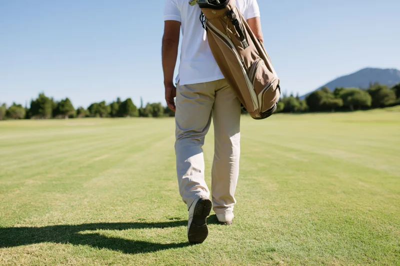 Man walking across a golf course fairway carrying a golf bag
