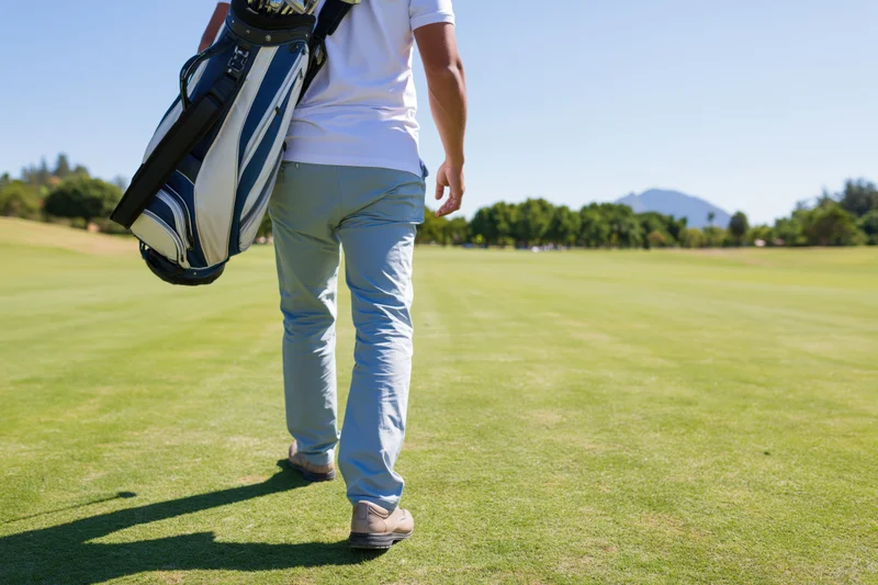Man walking across a golf course fairway carrying a golf bag