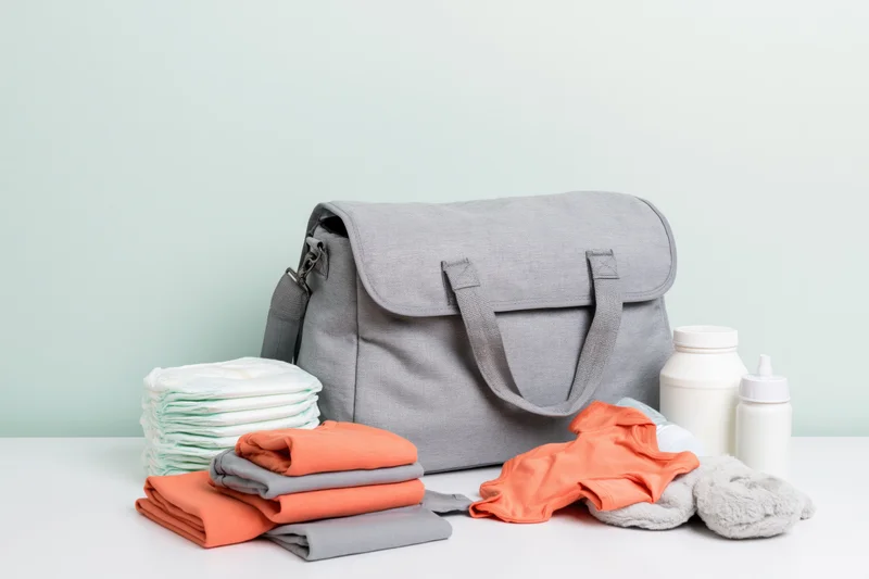 Grey diaper bag with baby essentials arranged on a white table