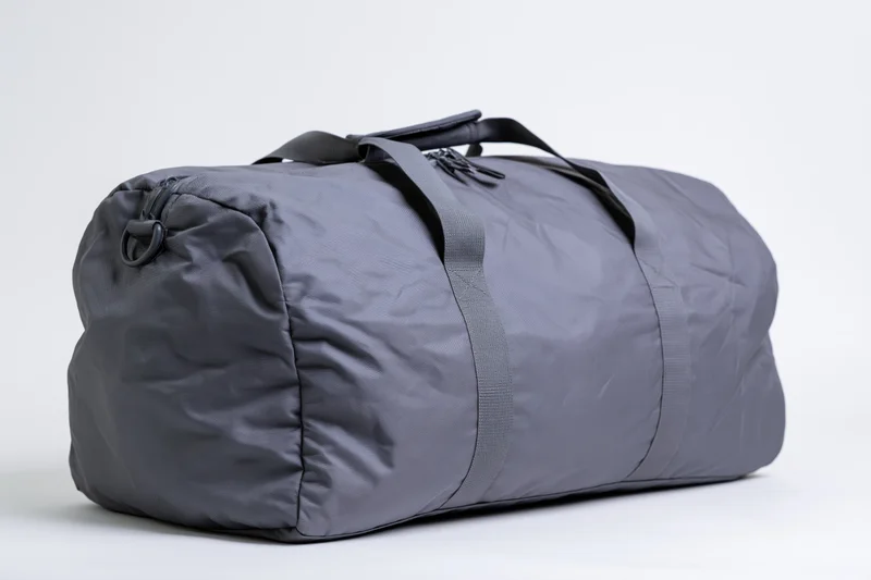 Grey nylon duffel bag with straps and zipper closure on white background