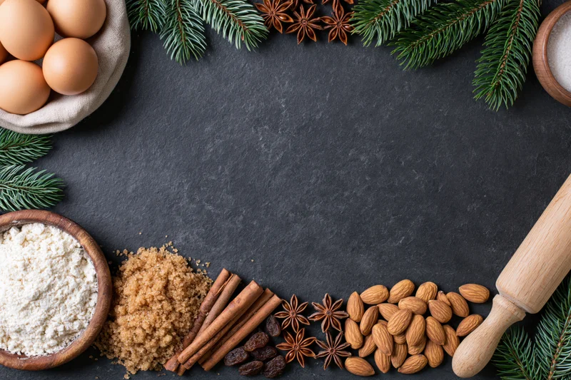 Holiday baking ingredients arranged along the bottom edge of a dark slate surface with copyspace above