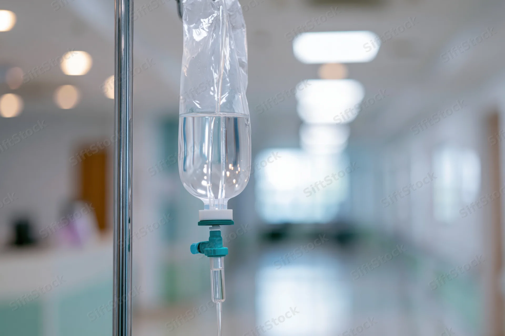 Iv saline drip bag hanging from stainless steel pole in hospital corridor