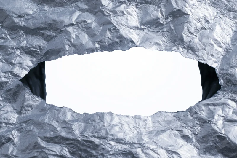 View through a torn rectangular hole in crumpled aluminum foil with white copyspace inside