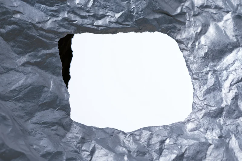 View through a torn rectangular hole in crumpled aluminum foil with white copyspace inside