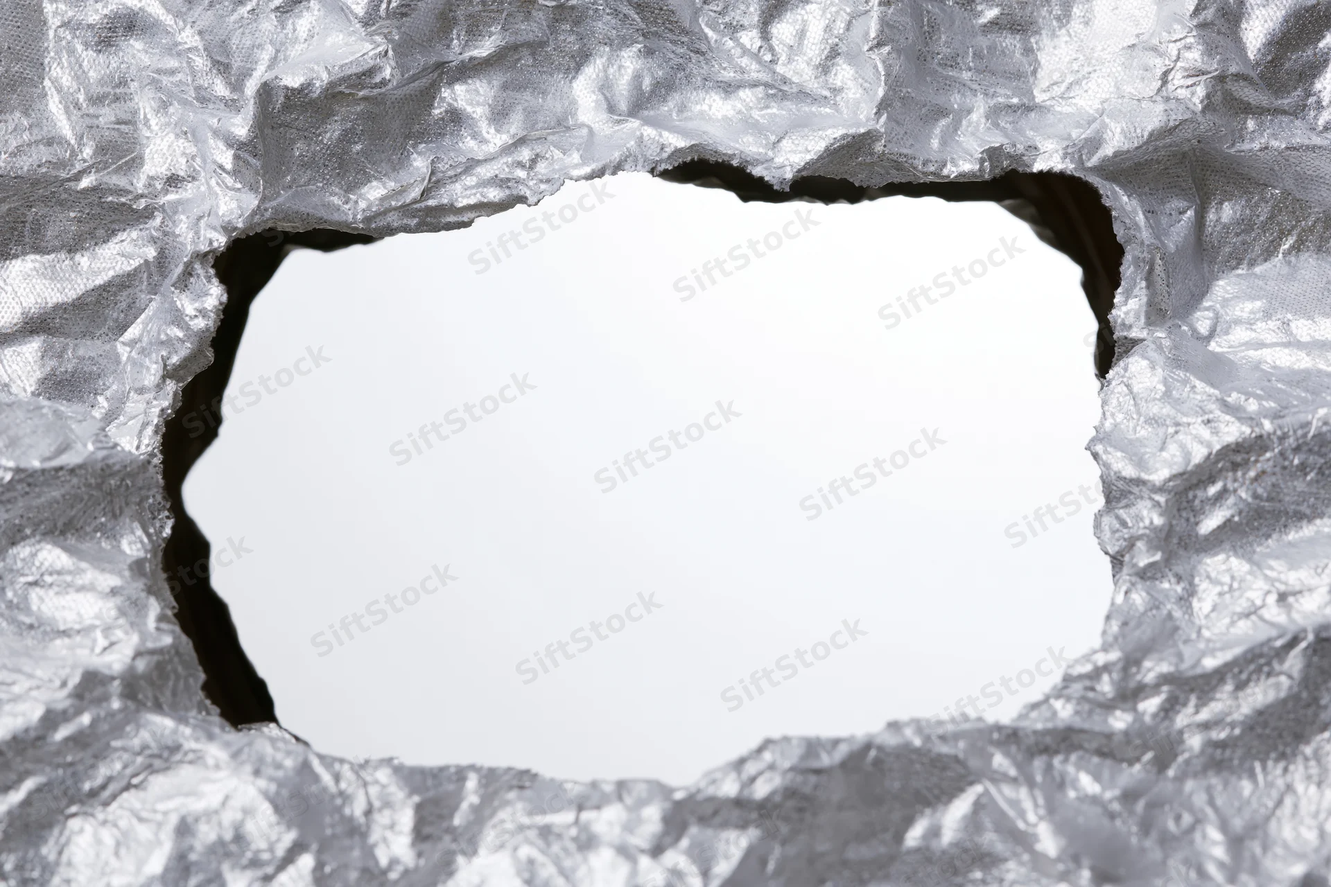 Torn rectangular hole in crumpled aluminum foil revealing white background