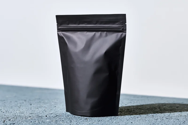 Matte black standup coffee pouch with zip closure on textured surface