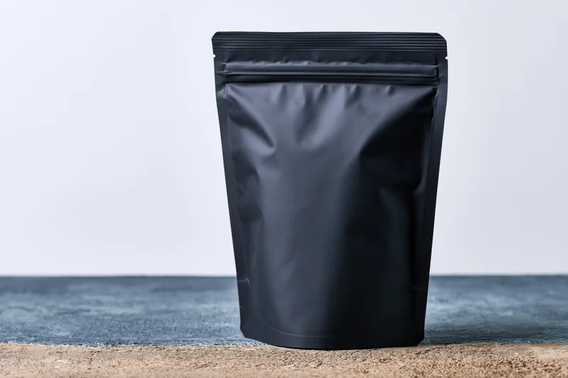 Matte black standup coffee pouch with zip closure on textured surface