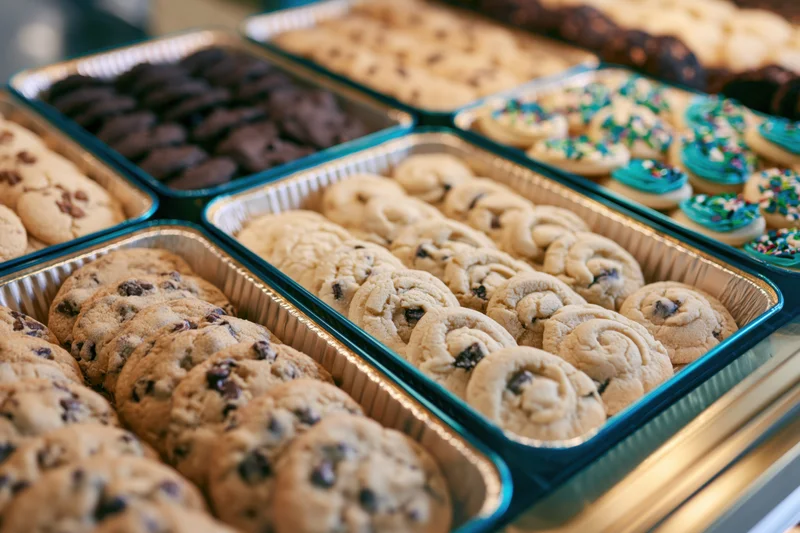 Assorted cookies in aluminum trays displayed on a bakery counter