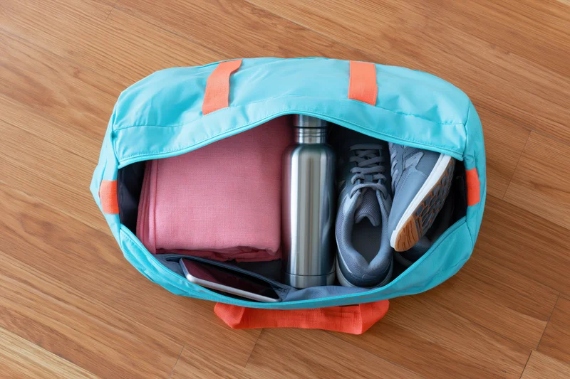 Open aqua-blue gym duffel bag with orange straps showing packed workout gear on wooden floor