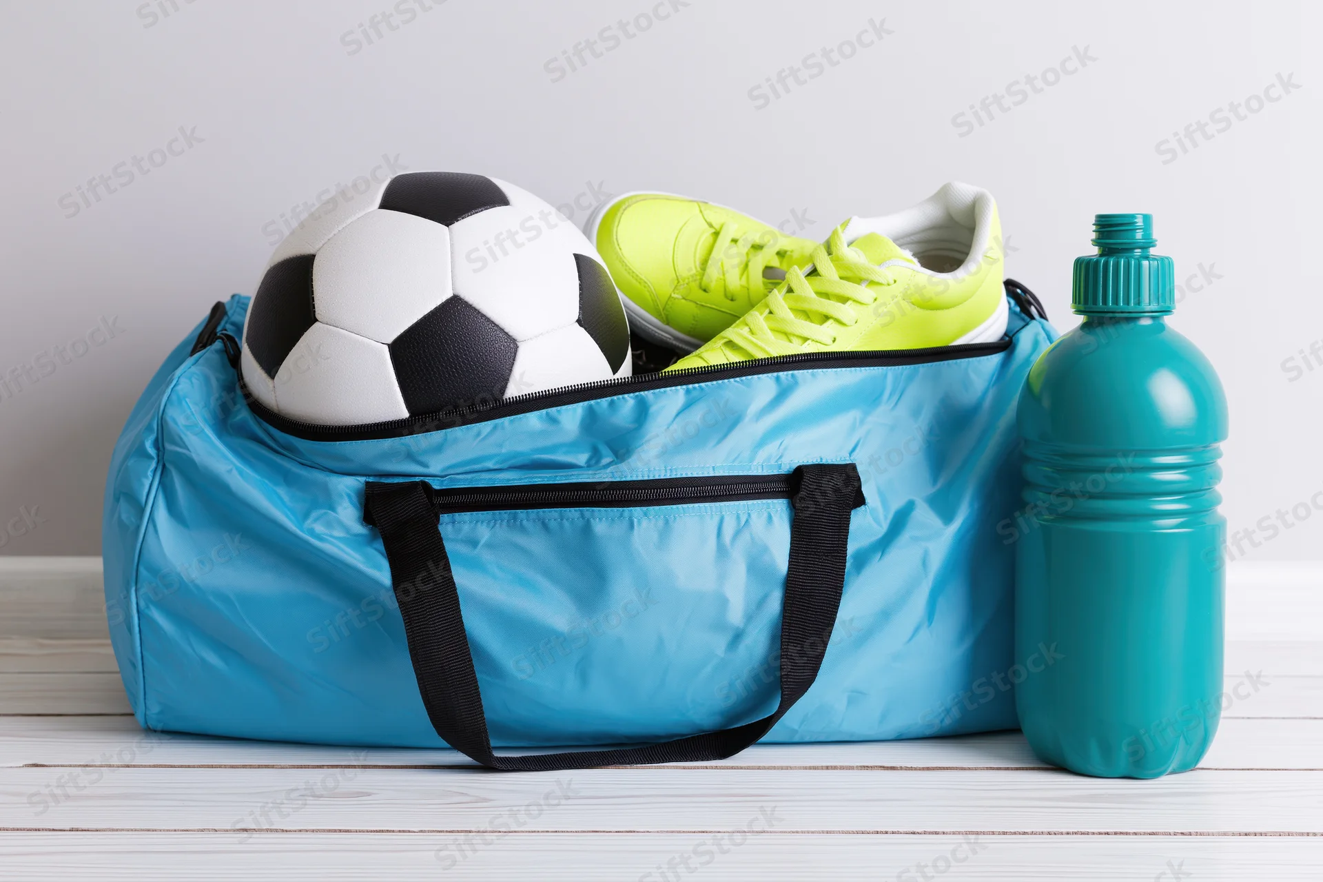 Cyan duffel bag with soccer ball and lime green cleats on wooden floor beside water bottle