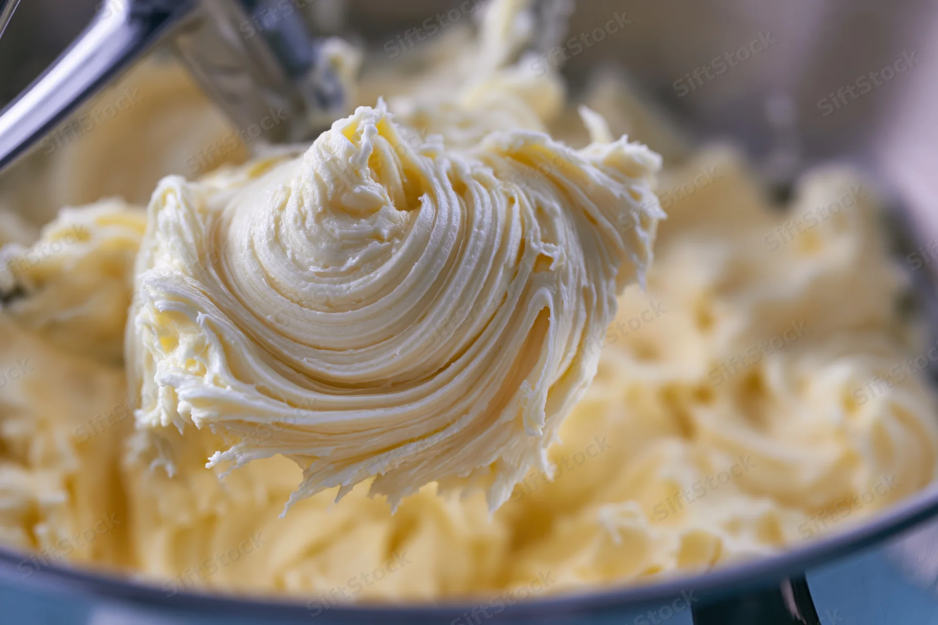 Pale yellow buttercream frosting being whipped in a stand mixer bowl