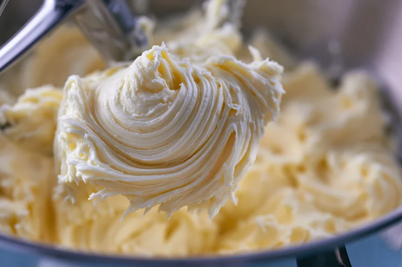 Pale yellow buttercream frosting being whipped in a stand mixer bowl