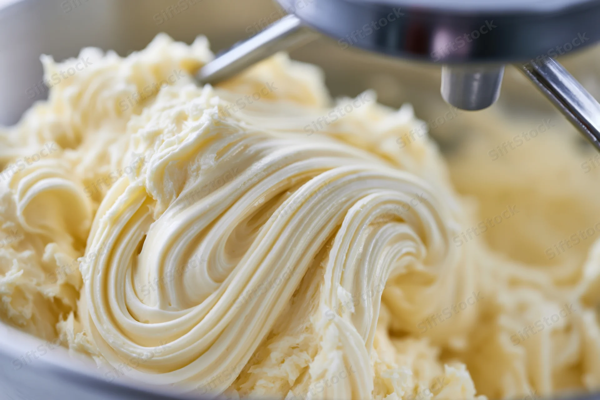 Pale yellow buttercream frosting being mixed in a stand mixer bowl