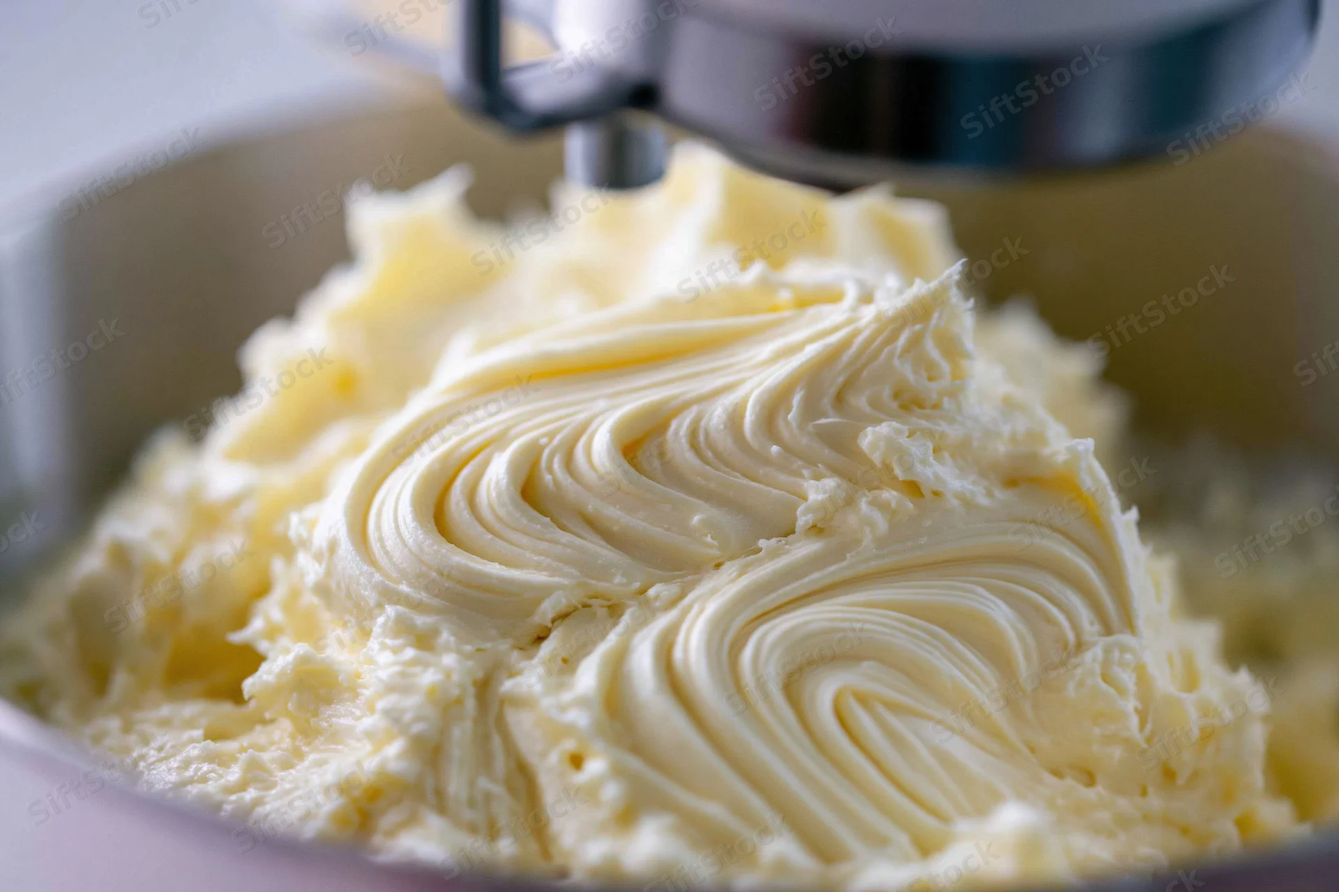 Pale yellow buttercream frosting being mixed in a stand mixer bowl