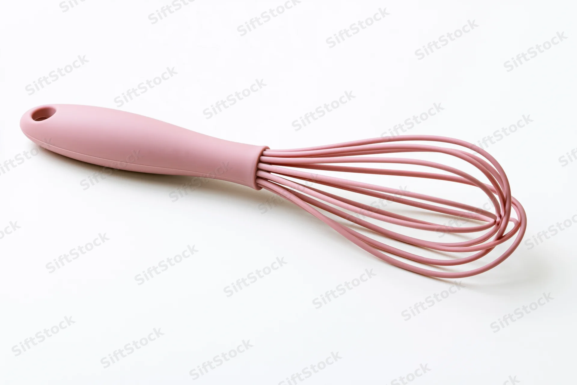 Pink silicone balloon whisk lying diagonally on white background