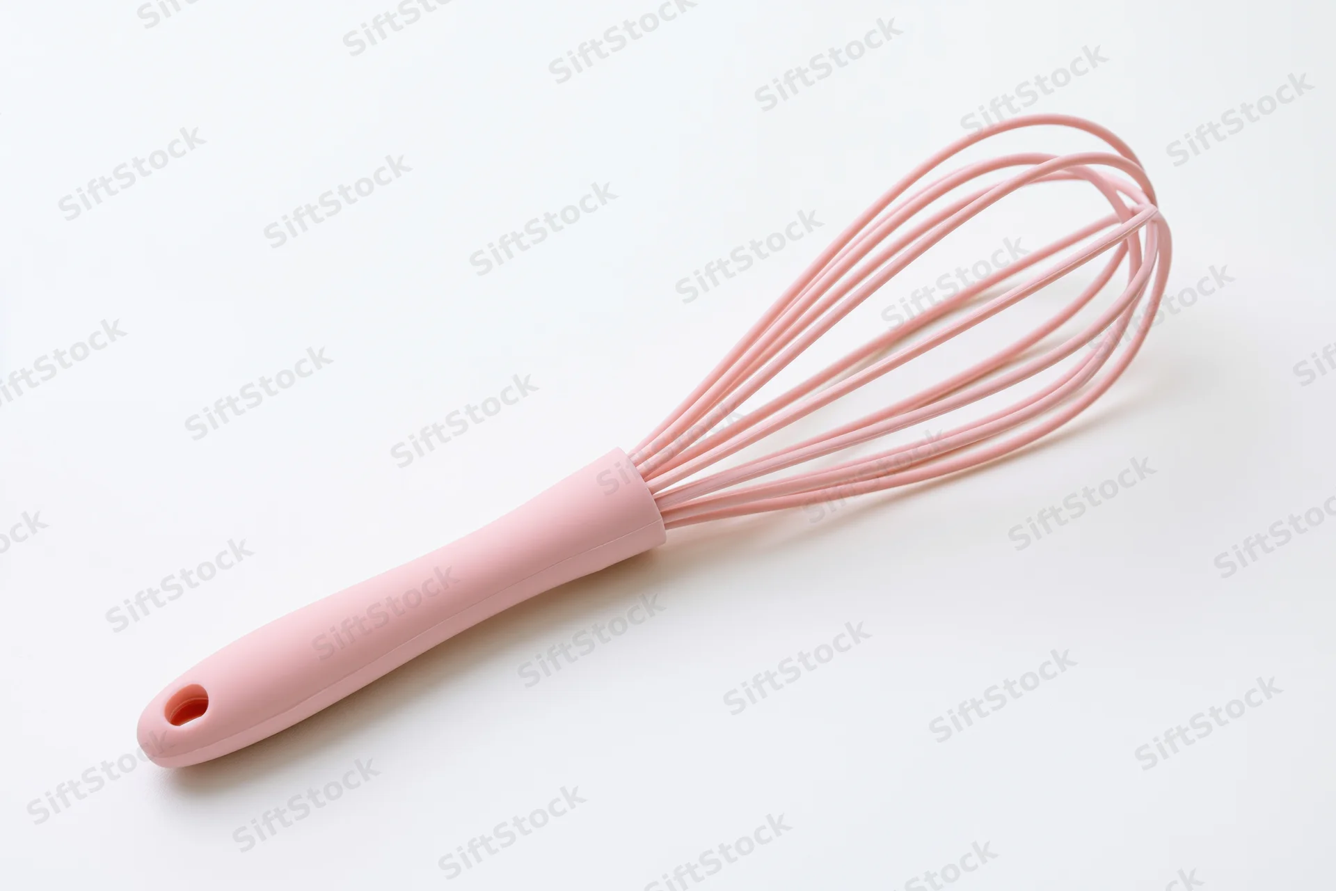 Pink silicone balloon whisk lying diagonally on white background